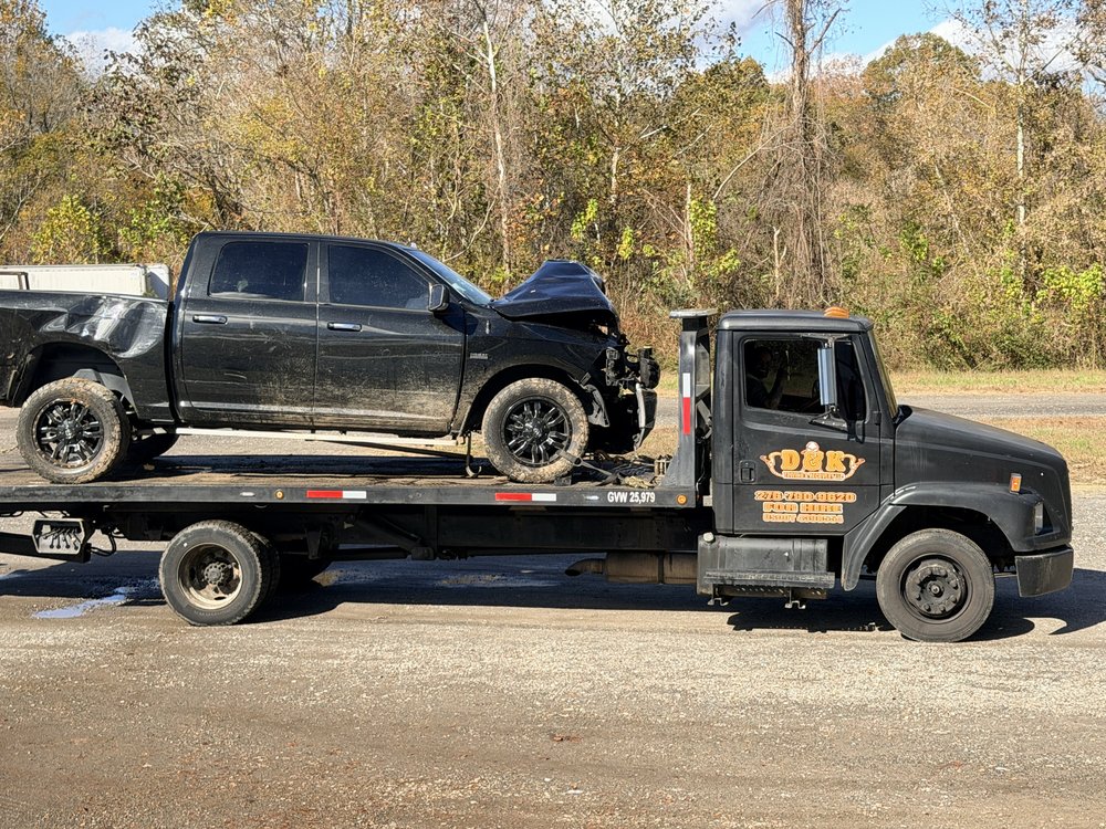 D&K Towing flatbed hauling a wrecked black pickup truck