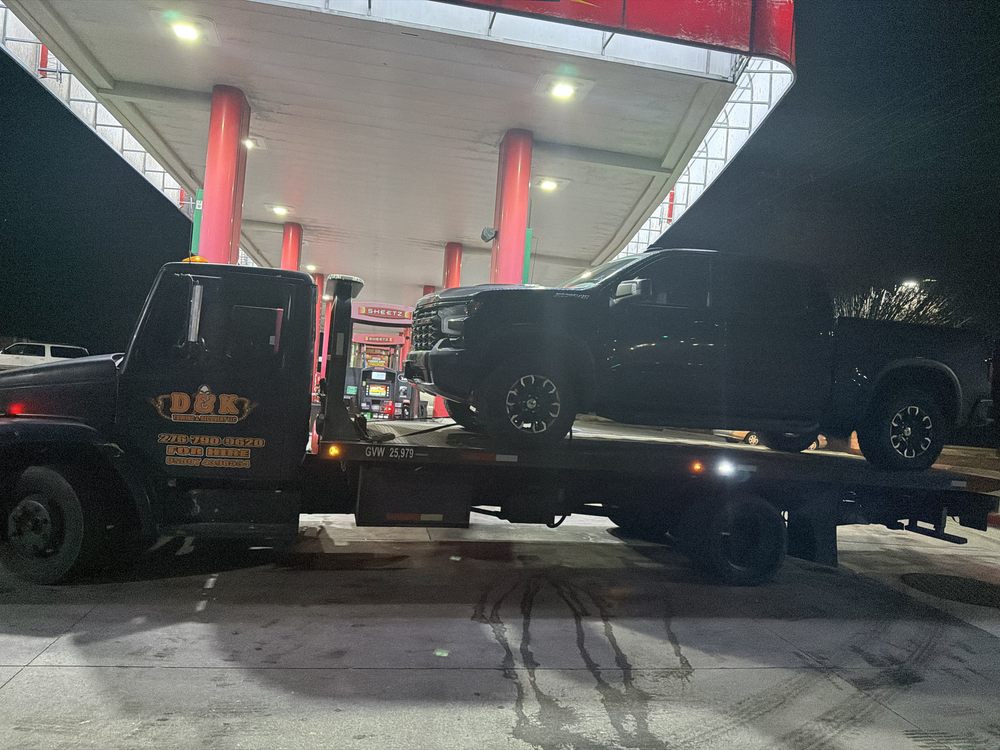 D&K tow truck hauling a pickup truck at a fuel station late at night
